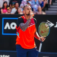 Australijski tenisista Nick Kyrgios z palcem na ustach, trzymający rakietę na korcie.