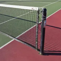 Siatka tenisowa na korcie, jej standardowa wysokosc siatki tenis jest kluczowa dla gry. Cień siatki pada na czerwoną nawierzchnię.
