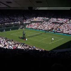 Widok na kort tenisowy podczas Wimbledonu, najstarszego turnieju tenisowego, z trybunami wypełnionymi widzami.